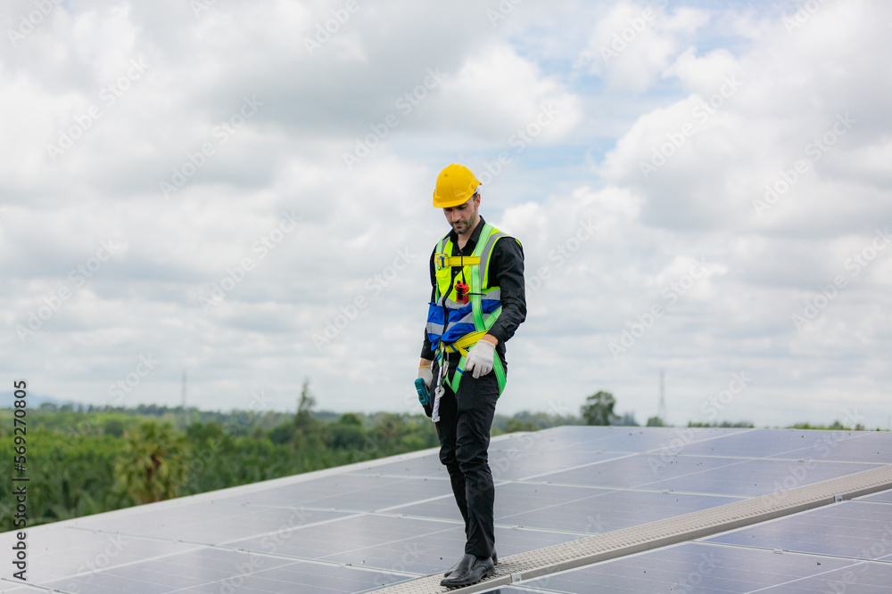 Obraz premium Handsome young male engineer wearing safety vest and jacket with gloves and tools along with hard hat helmet standing on solar panel while checking and looking at its maintenance