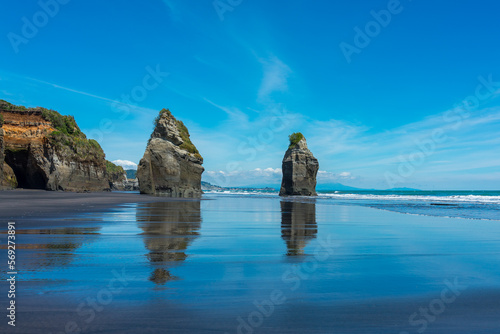 Strand mit schwarzem Sand und Spiegelung und Wellen und Felsen in Neuseeland bei den Three Sisters.