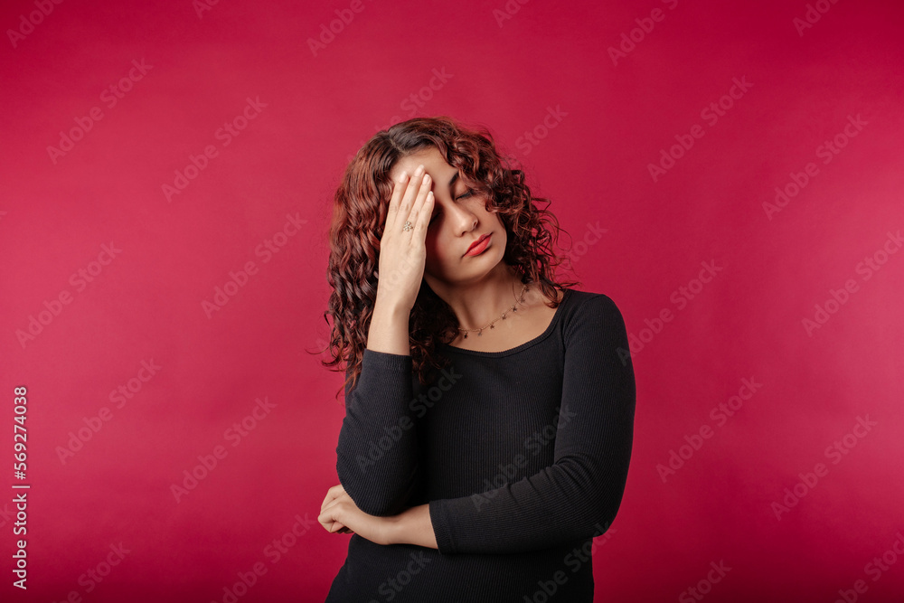 Woman wearing black dress standing isolated over red background feeling bad sick covering forehead with hand. Touching forehead having headache migraine or depression, upset frustrated troubled. Woman wearing black dress standing isolated over red background feeling bad sick covering forehead with hand. Touching forehead having headache migraine or depression, upset frustrated troubled.