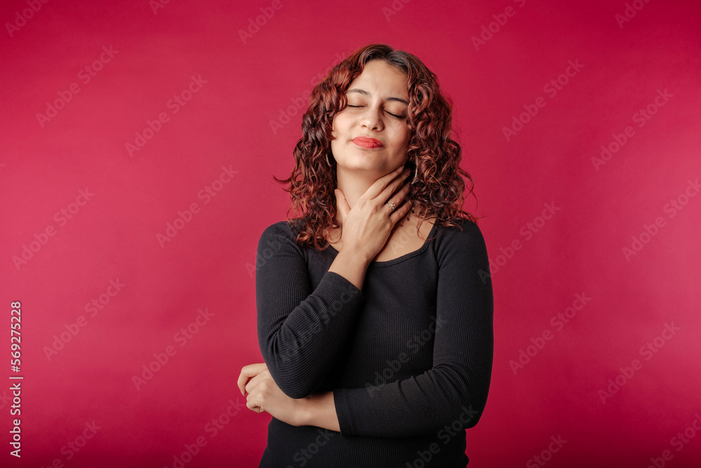 Woman standing isolated over red background holding her inflamed throat. Medical concept, Sore throat. Having sore throat, holding hand on her neck, suffering from throat pain, painful swallowing. Woman standing isolated over red background holding her inflamed throat. Medical concept, Sore throat. Having sore throat, holding hand on her neck, suffering from throat pain, painful swallowing.