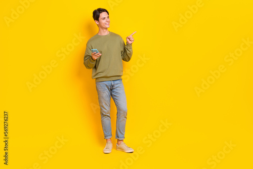 Full size portrait of positive nice man hold telephone direct finger empty space isolated on yellow color background © deagreez
