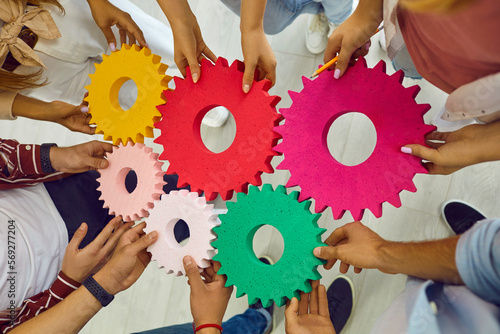 Team of people, students or corporate workers, standing in circle, holding colorful cogs and joining them. Cropped shot of hands with gears. Teamwork, business, education, success concept background