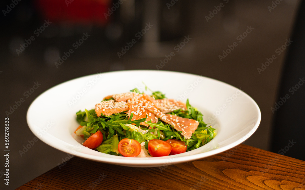 White ceramic plate of fresh salad with salmon, vegetables, tomatoes and arugula with sesame seeds. White ceramic plate of fresh salad with salmon, vegetables, tomatoes and arugula with sesame seeds.