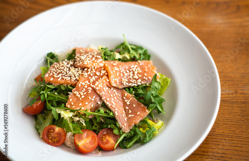 White ceramic plate of fresh salad with salmon, vegetables, tomatoes and arugula with sesame seeds. (ID: 569278600)
