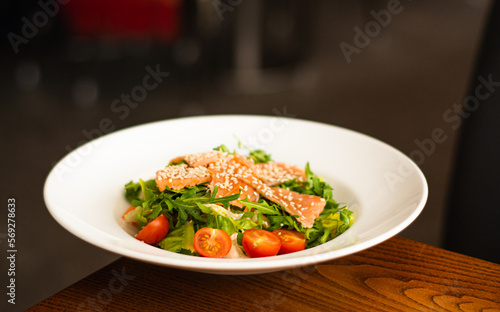 White ceramic plate of fresh salad with salmon, vegetables, tomatoes and arugula with sesame seeds. (ID: 569278633)