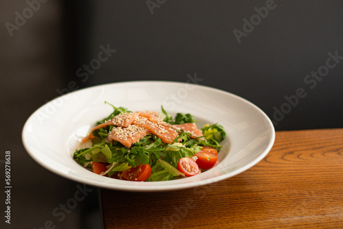 White ceramic plate of fresh salad with salmon, vegetables, tomatoes and arugula with sesame seeds. (ID: 569278638)