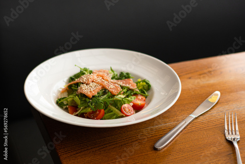 White ceramic plate of fresh salad with salmon, vegetables, tomatoes and arugula with sesame seeds. (ID: 569278652)