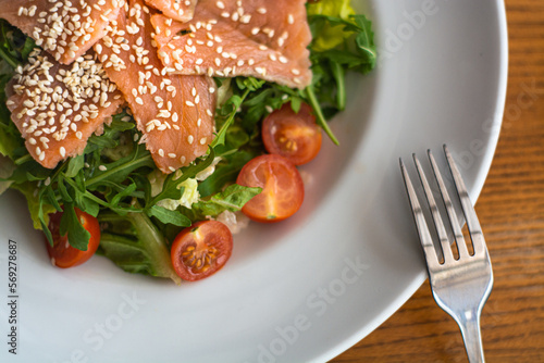 White ceramic plate of fresh salad with salmon, vegetables, tomatoes and arugula with sesame seeds. (ID: 569278687)