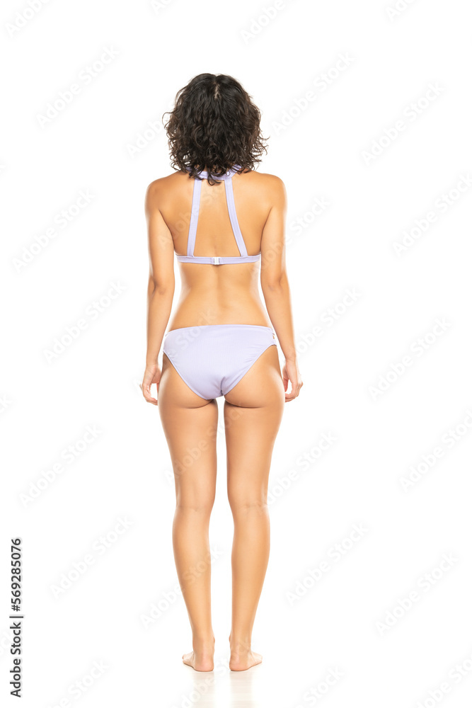 Young brunette woman in lilac bikini swimsuit posing on a white background.  Back, rear view. Stock Photo