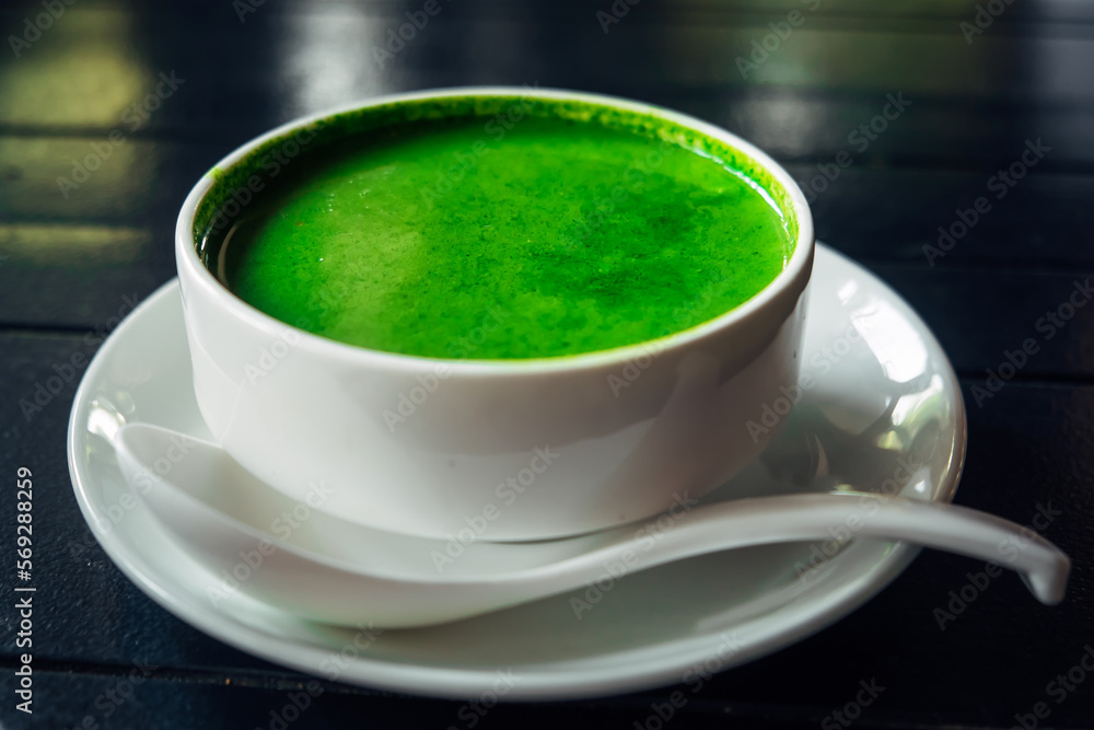 Green spinach soup in a white round plate with a spoon on a dark background. Vegetarian food