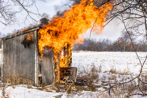 Fotografie A two door outhouse or small shed on fire in the winter with large flames