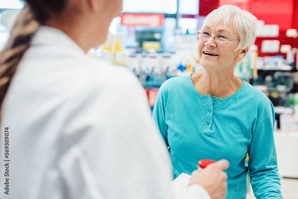 Pharmacist servicing senior customer in her pharmacy holding bottle with pills in her hand