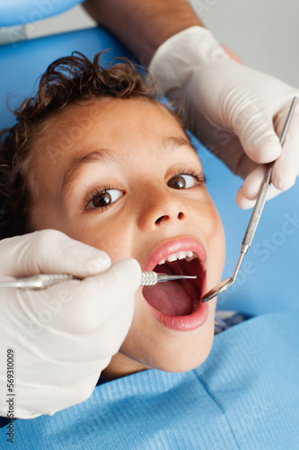 Crop dentist examining teeth of boy. anonymous dentist in gloves using tooth on teeth of little patient while cute boy looking at camera during checkup procedure