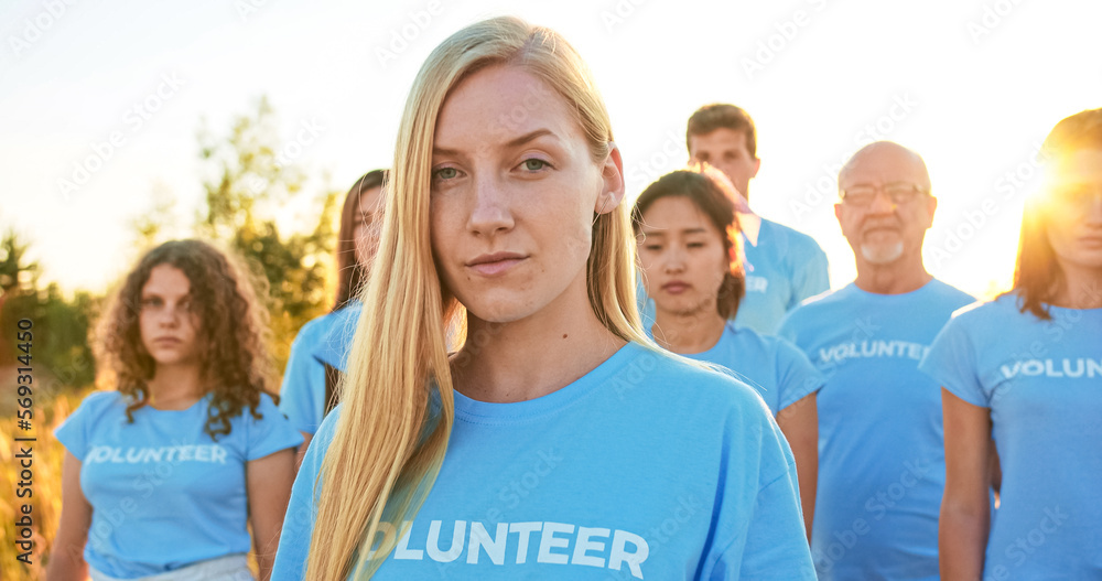 Young attractive woman with a group of eco activists in the background. Pretty Caucasian female volunteer looking at camera and saying: I Am a Volunteer. Volunteering, environmental conservation. Young attractive woman with a group of eco activists in the background. Pretty Caucasian female volunteer looking at camera and saying: I Am a Volunteer. Volunteering, environmental conservation.