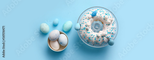 Tasty Easter cake and painted eggs on light blue background