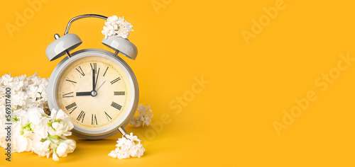 Alarm clock and flowers on orange background with space for text. Spring time