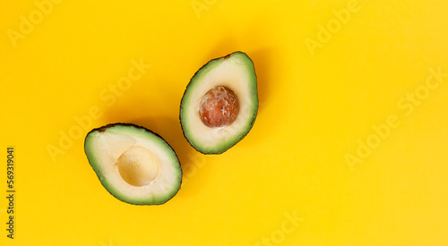 Organic avocado with seed, avocado halves and whole fruits on yellow background. Top view. Pop art design, creative summer food concept. Green avocadoes pattern in minimal flat lay style
