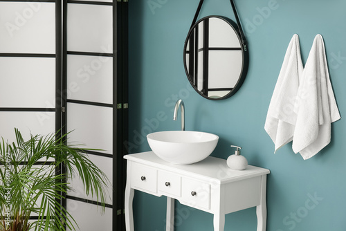 Table with drawers  sink and mirror hanging on blue wall in bathroom