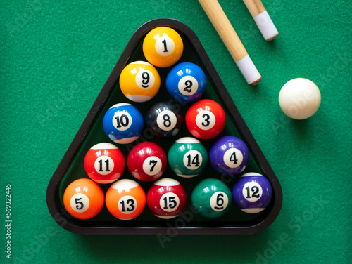 Spots and stripes balls in triangle, cue ball and two cues on the green table. Mini billiard, pool or snooker photo