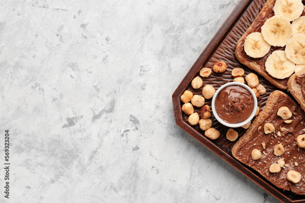 Wooden board of tasty toasts with hazelnut butter, banana and nuts on light background Wooden board of tasty toasts with hazelnut butter, banana and nuts on light background