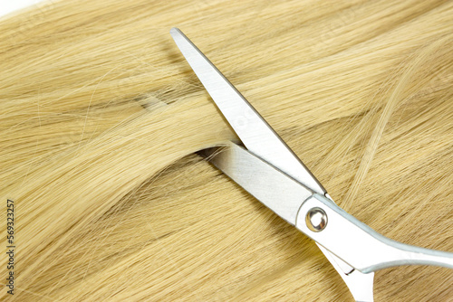 Flat lay composition with light blond hair, scissors and space for text on white background.Top view of healthy blond hair lock extension and hairdresser scissors on white background.