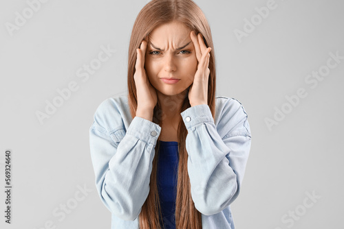Young woman suffering from loud noise on grey background
