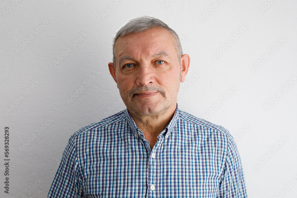Portrait of a gray-haired elderly man in a blue shirt, isolated indoors on a white background. Portrait of a gray-haired elderly man in a blue shirt, isolated indoors on a white background.
