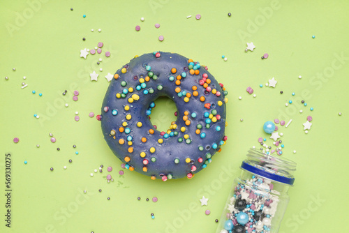 Delicious donut and overturned jar of sprinkles on green background
