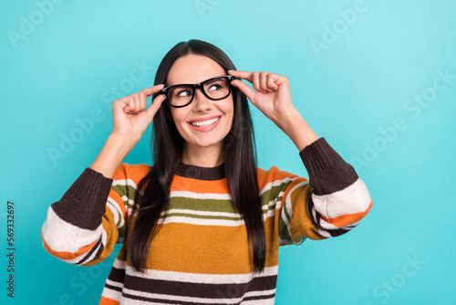 Photo of young seo manager positive lady wear striped orange sweater touch eyeglasses look empty space new vacancy isolated on cyan color background
