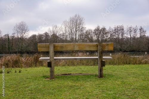 empty wooden bench in park facing lake. A lonely bench during cold winter day. 