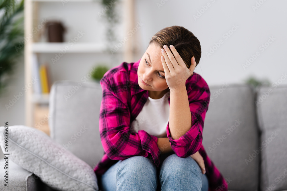 Sad young woman suffering depression hand on head sitting on couch ...
