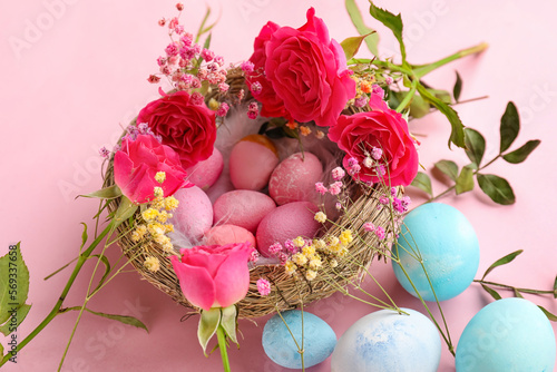 Nest with painted Easter eggs and flowers on pink background  closeup