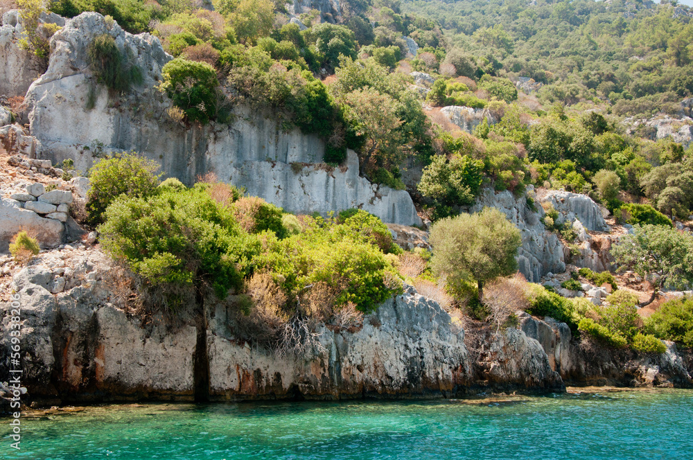 Sunken Lycian city on the Kekova island, Turkey. Green trees, old stone houses damaged by earthquake. Ruins in the Mediterranean Sea. Sunny summer day landscape. Selective focus