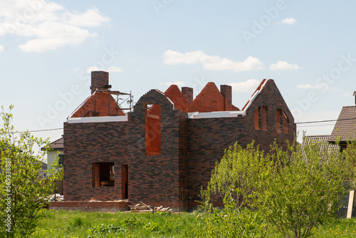Facade of new brick house without roof during construction among green landscape