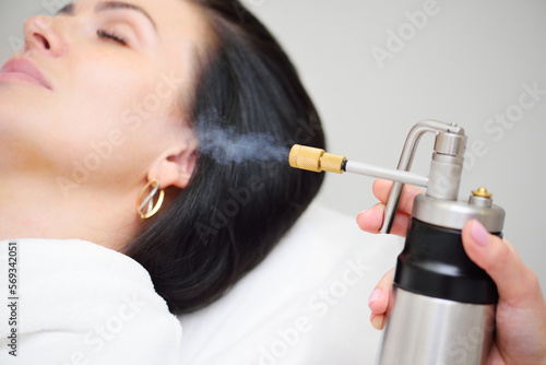 cosmetologist makes a cryomassage of the face to the patient – a cosmetological procedure of exposure to the skin with liquefied nitrogen using a cryodestructor apparatus