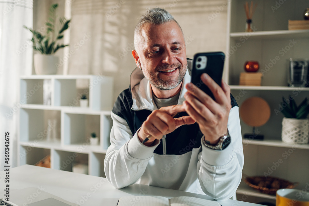 Middle aged man talking on a smartphone while working in a home office Middle aged man talking on a smartphone while working in a home office