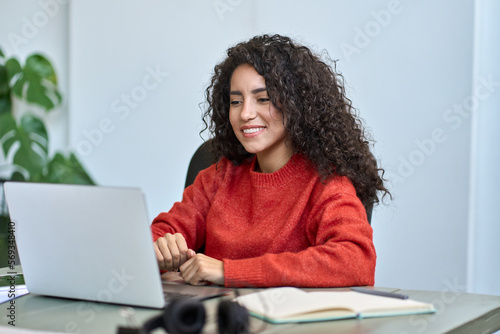 Tableau sur toile Young happy latin business woman employee using laptop, having remote virtual work meeting call in office or watching webcast online webinar training web course looking at computer sitting at desk