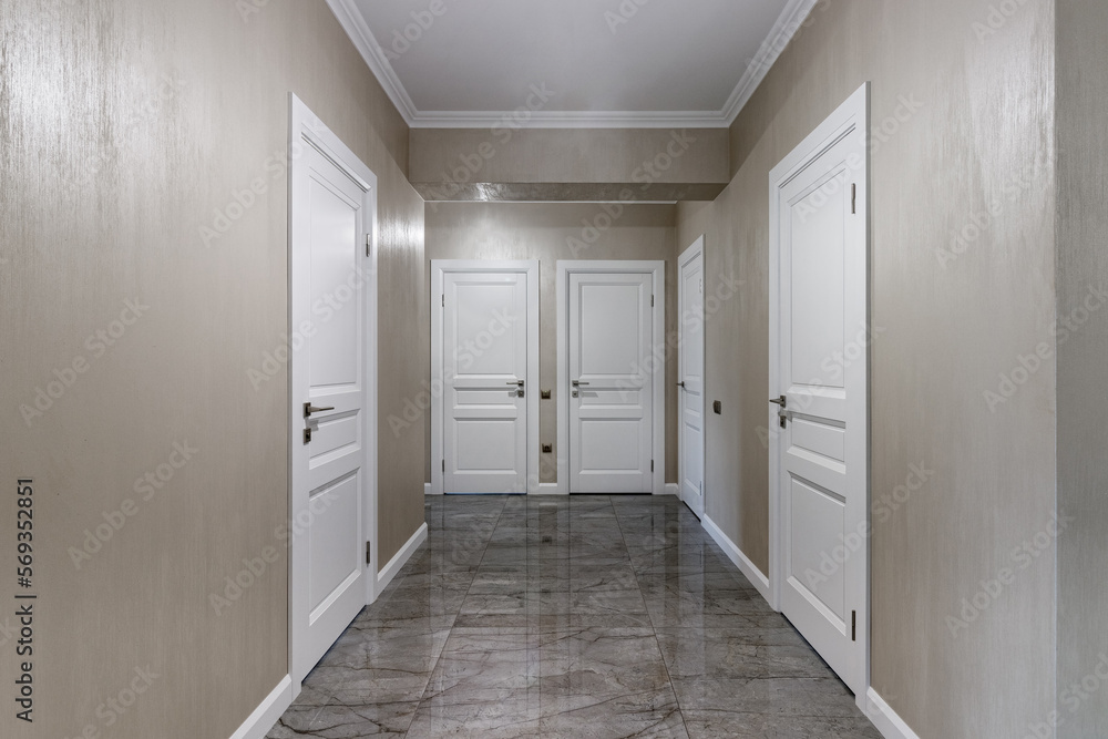 Corridor with white walls and doors in an apartment with a marble floor Corridor with white walls and doors in an apartment with a marble floor