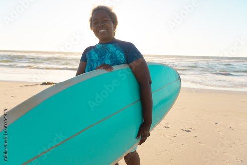 Senior african american senior woman with surfboard enjoying on sandy beach against sea and sky