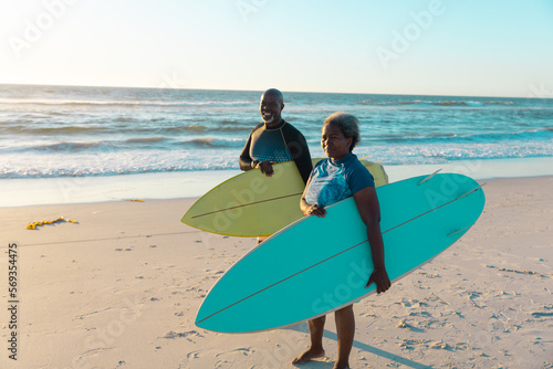 Senior frican american couple with surfboards standing at sandy beach against sea and sky