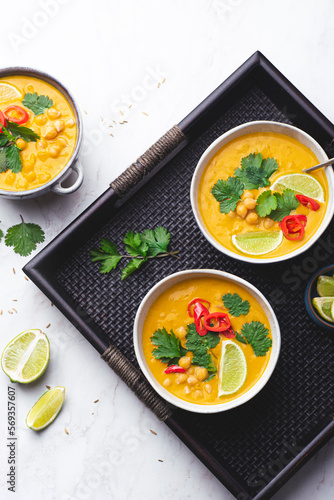 Light orange veggie curry with chickpeas, chili peppers, coriander leaves and cumin seeds on a wicker ethnic tray. Vegetarian recipes, healthy food Fusion cuisine