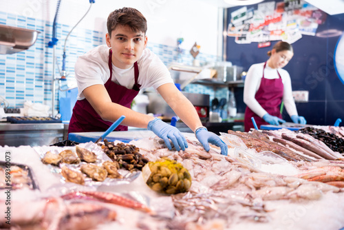 Positive young salesman demonstrating fresh calamary behind counter in fish store