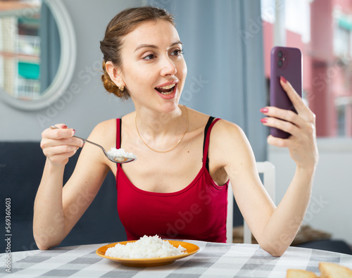 Positive woman eating portion of boiled rice at home and taking selfies.