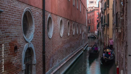 Canal in Venice timelapse with gongolas passing by. Channel, bridges, historical old houses and boats. Scenic cityscape view with tower on background. Venice, Italy. Blue sky at summer day photo