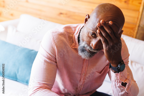 Close-up of stressed bald african american senior man with head in hand sitting on sofa in log cabin