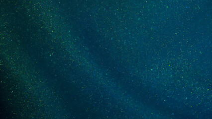 Magical green curtain with golden sequins. Green background with golden glittering dust particles and iridescent depth of field. Abstract green background with tints of gold sparkles and blue shades.