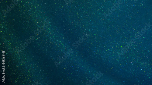 Magical green curtain with golden sequins. Green background with golden glittering dust particles and iridescent depth of field. Abstract green background with tints of gold sparkles and blue shades.