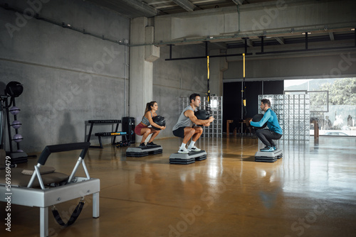 Sporty man and woman doing squats with medicine ball in big gym. Copy space, wide angle