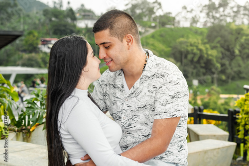 beautiful young latin couple in love, in an outdoor park looking into each other's eyes while smiling.