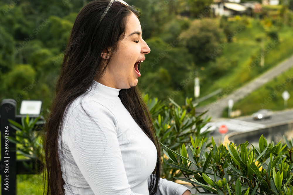 young latina woman, yawning in an outdoor park. very sleepy and tired. young latina woman, yawning in an outdoor park. very sleepy and tired.